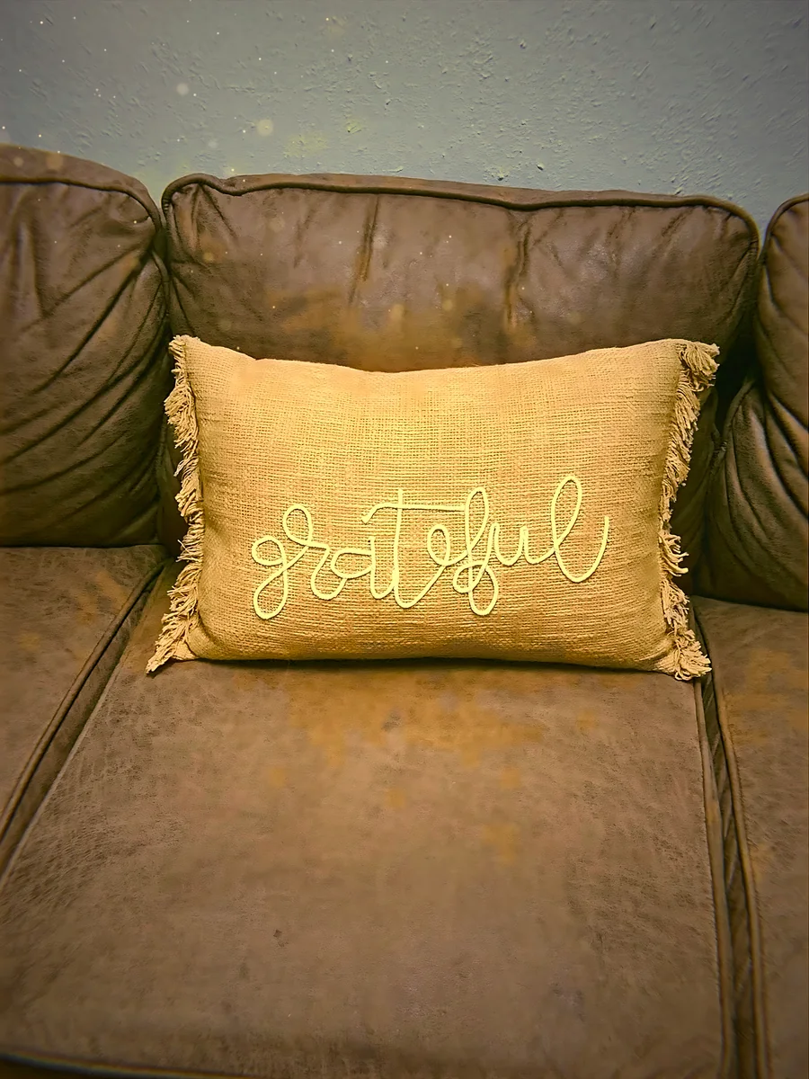 A mustard Grateful pillow on a leather sofa