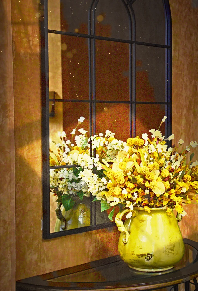 A sunlit bouquet in a green pitcher before an arched mirror in the Grace Wellness lobby