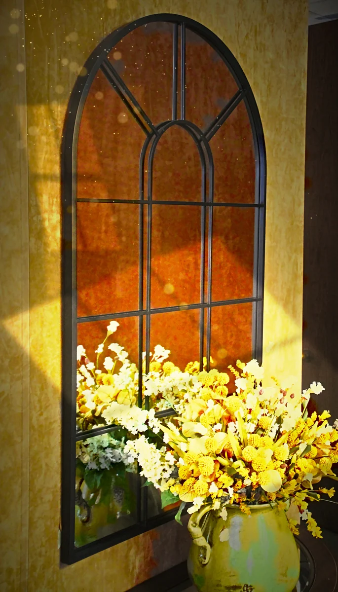 A fall flower arrangement in front of an arched mirror