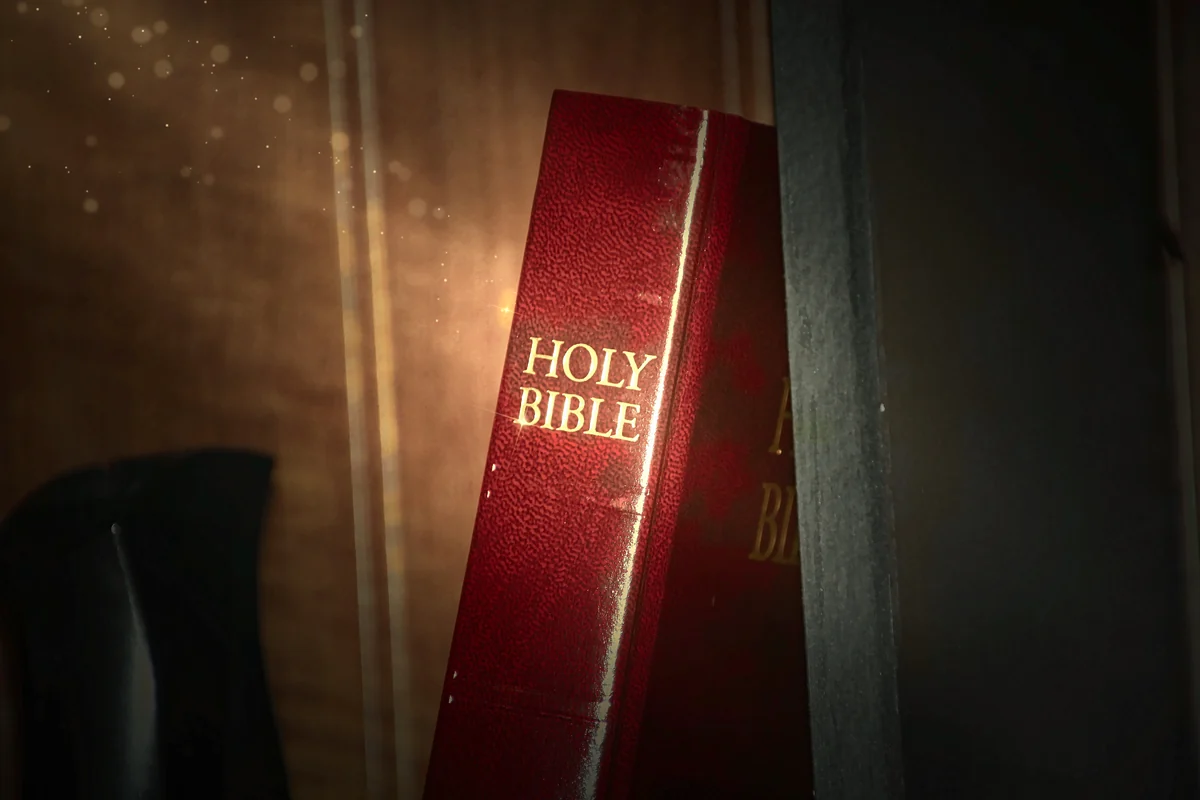 A red Holy Bible on a wooden shelf in afternoon sun